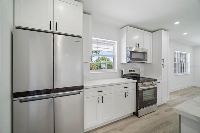 kitchen featuring white cabinets, stainless steel appliances, light stone countertops, and light hardwood / wood-style floors