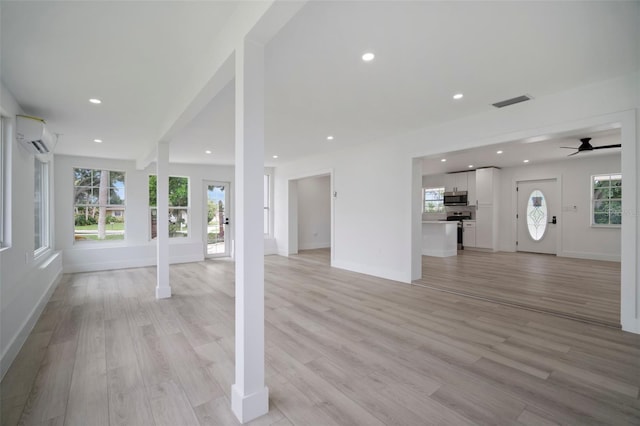 unfurnished living room with an AC wall unit, ceiling fan, and light hardwood / wood-style flooring