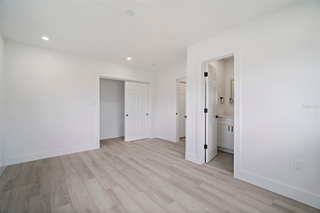 unfurnished bedroom featuring a closet, light wood-type flooring, and ensuite bath