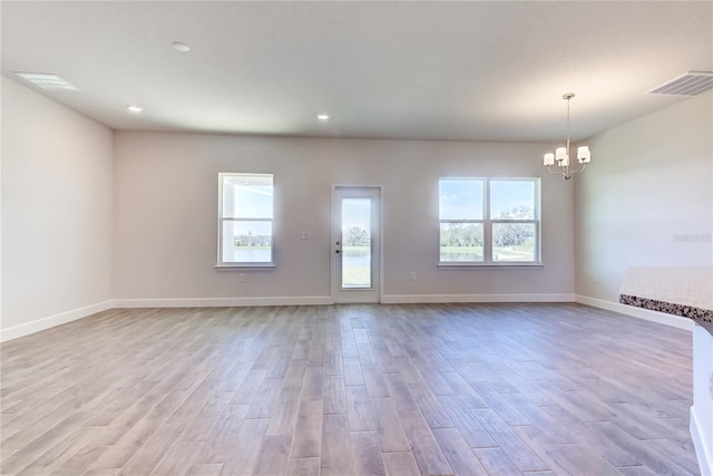 spare room featuring plenty of natural light, an inviting chandelier, and light hardwood / wood-style floors