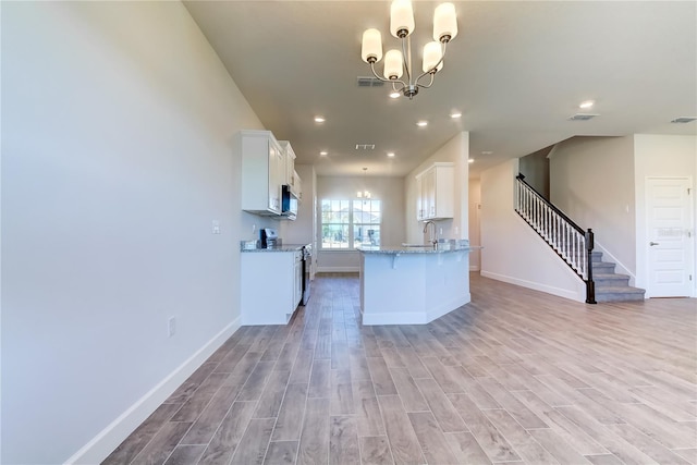 kitchen with stainless steel range with electric stovetop, light stone countertops, white cabinets, a chandelier, and light wood-type flooring