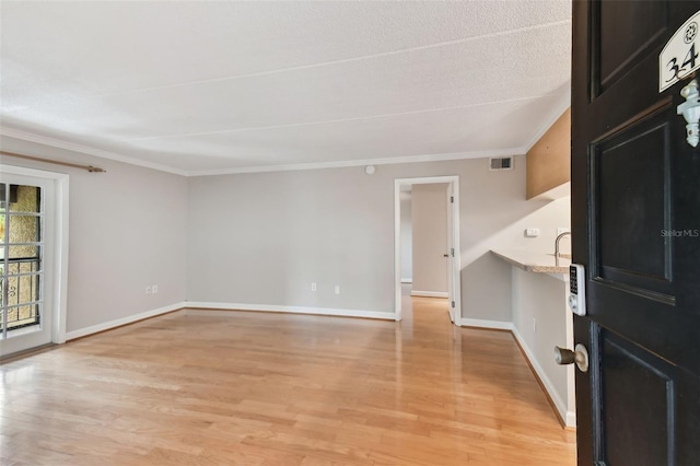 empty room featuring baseboards, light wood finished floors, visible vents, and crown molding