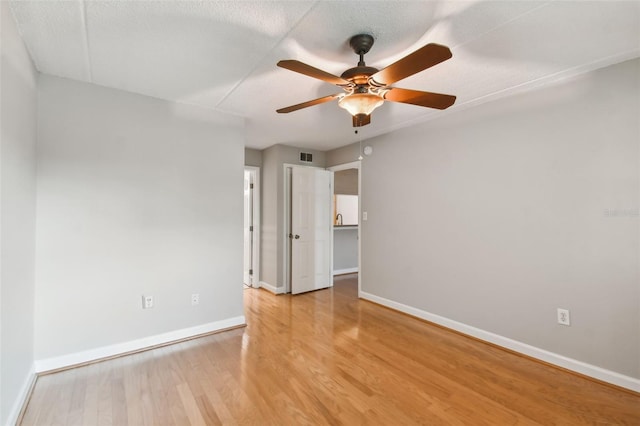 empty room featuring visible vents, light wood-style floors, a ceiling fan, a textured ceiling, and baseboards