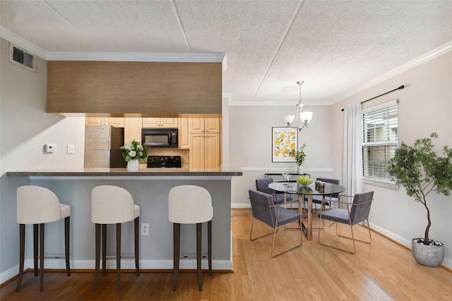 kitchen with dark countertops, hanging light fixtures, light wood-style floors, black appliances, and a kitchen breakfast bar