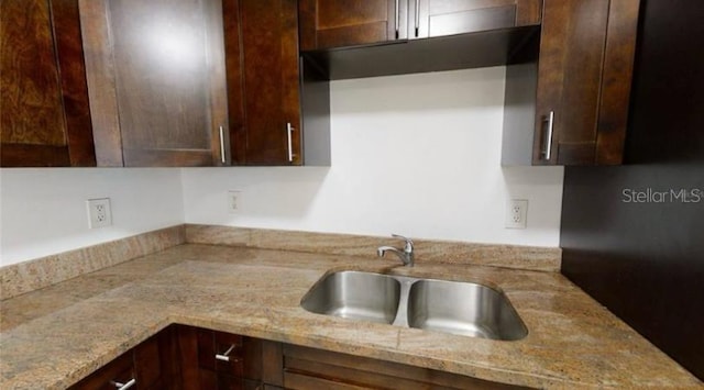 kitchen featuring dark brown cabinetry, light stone counters, and sink