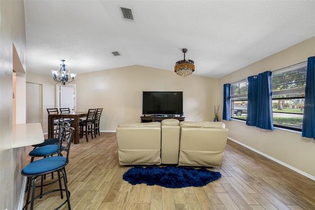 living room featuring a notable chandelier, light wood-type flooring, a textured ceiling, and vaulted ceiling