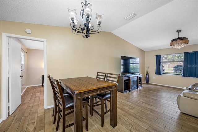 dining area featuring hardwood / wood-style floors, lofted ceiling, a textured ceiling, and a chandelier