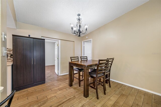 dining space featuring a chandelier, lofted ceiling, a textured ceiling, and light hardwood / wood-style flooring