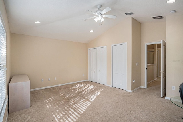 unfurnished bedroom with ceiling fan, light colored carpet, high vaulted ceiling, and multiple closets