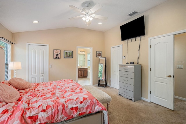 bedroom with ensuite bath, ceiling fan, light colored carpet, vaulted ceiling, and two closets