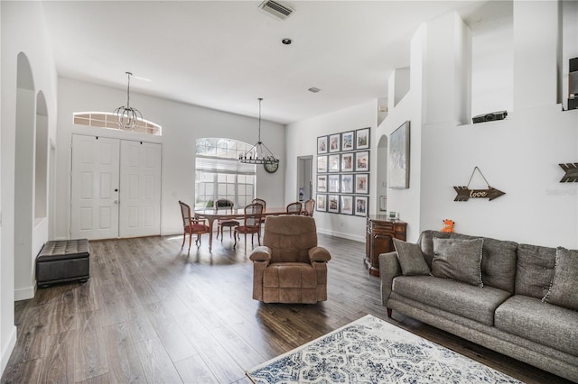 living area with wood finished floors, baseboards, visible vents, arched walkways, and an inviting chandelier