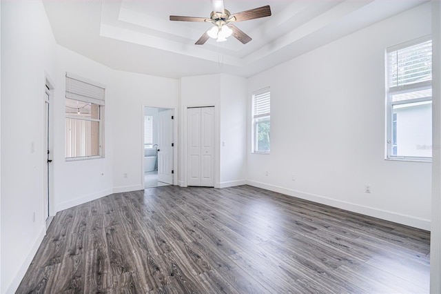 unfurnished bedroom with baseboards, ceiling fan, dark wood-type flooring, and a raised ceiling