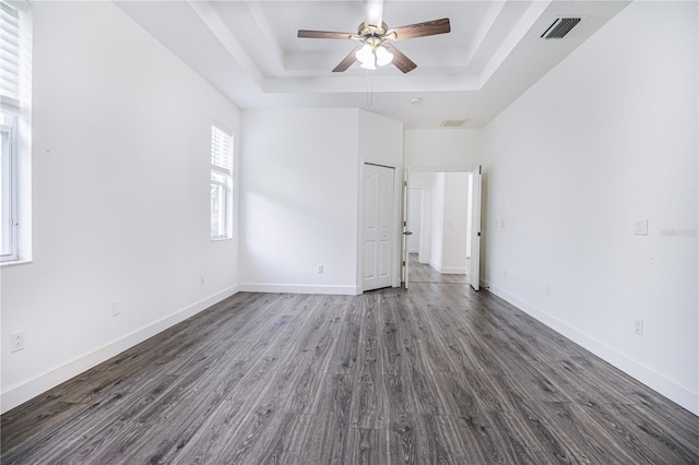 unfurnished bedroom with a tray ceiling, baseboards, dark wood-type flooring, and visible vents