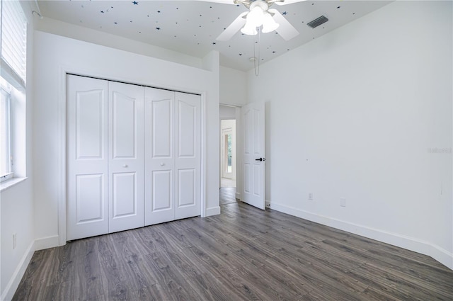 unfurnished bedroom featuring ceiling fan, a towering ceiling, hardwood / wood-style flooring, and a closet