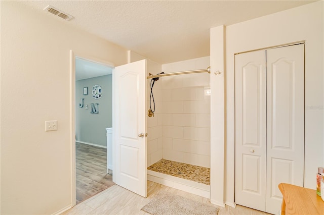 bathroom featuring hardwood / wood-style floors, tiled shower, and a textured ceiling