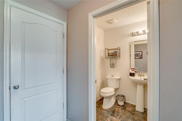 half bath featuring toilet, baseboards, and a sink