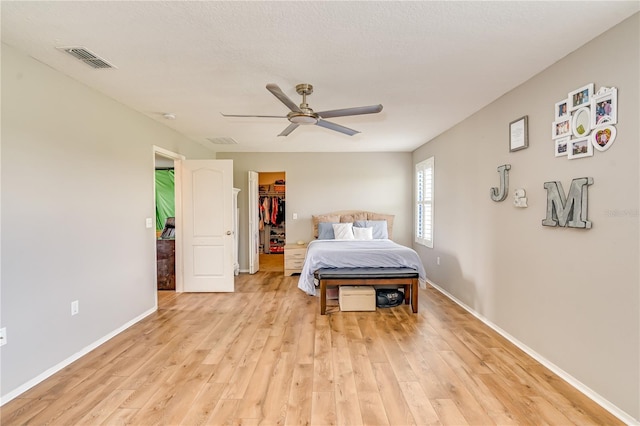 bedroom with a spacious closet, visible vents, light wood finished floors, and baseboards