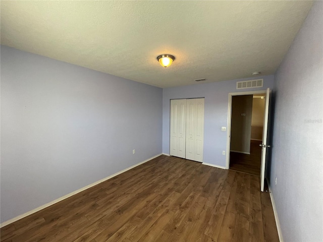 unfurnished bedroom featuring dark wood-style floors, baseboards, visible vents, and a closet