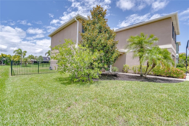 view of property exterior with a lawn, stucco siding, and fence