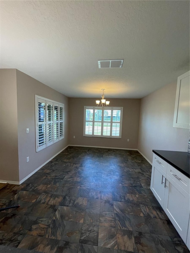 unfurnished dining area featuring a textured ceiling, stone finish floor, visible vents, baseboards, and a notable chandelier