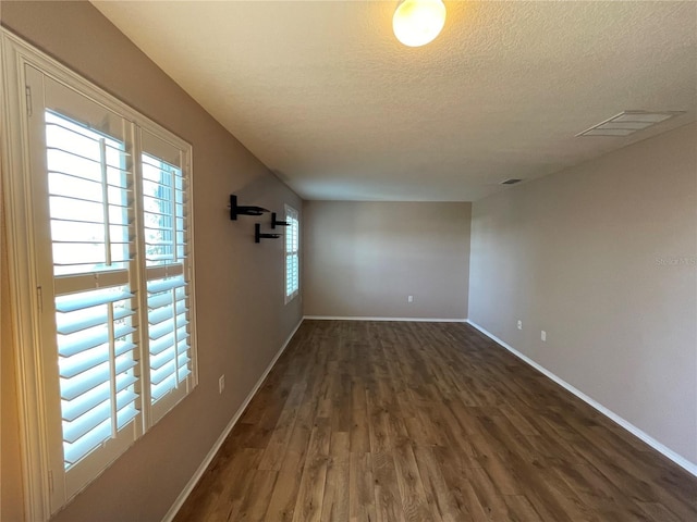 empty room with a textured ceiling, dark wood-style flooring, visible vents, and baseboards