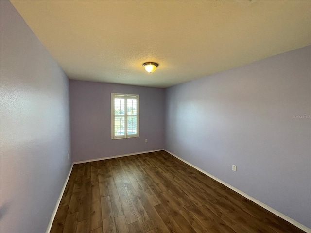 spare room with baseboards and dark wood-style flooring