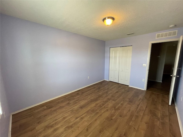 unfurnished bedroom with a closet, visible vents, baseboards, a textured ceiling, and wood finished floors