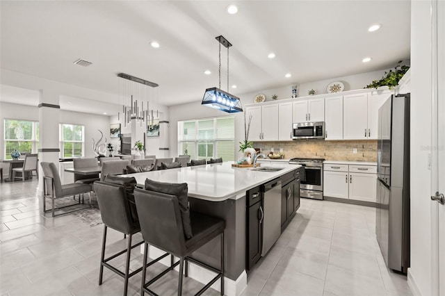 kitchen featuring a kitchen island with sink, white cabinets, stainless steel appliances, and decorative light fixtures