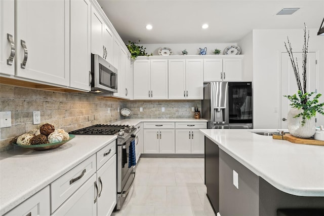 kitchen featuring tasteful backsplash, white cabinets, light tile patterned flooring, and appliances with stainless steel finishes