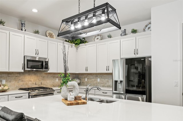 kitchen with backsplash, white cabinets, sink, appliances with stainless steel finishes, and decorative light fixtures