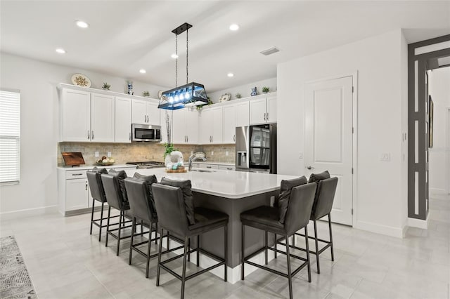 kitchen with white cabinets, appliances with stainless steel finishes, a kitchen island with sink, and hanging light fixtures