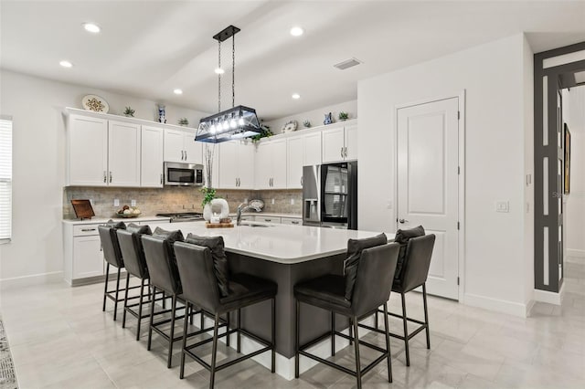 kitchen featuring white cabinetry, stainless steel appliances, pendant lighting, a breakfast bar area, and a center island with sink