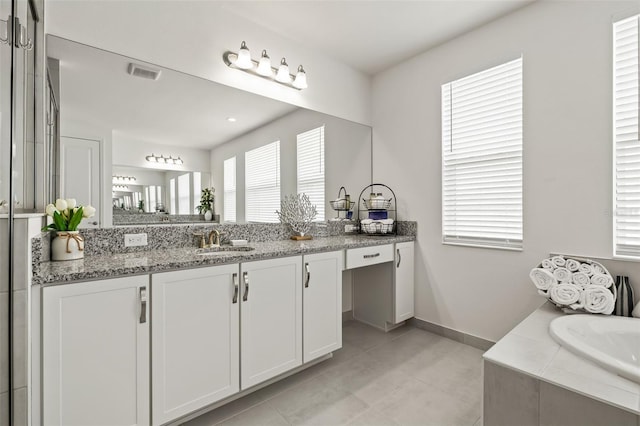 bathroom with tiled bath, a wealth of natural light, tile patterned flooring, and vanity