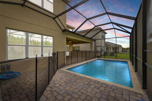 pool at dusk with a patio, glass enclosure, and ceiling fan