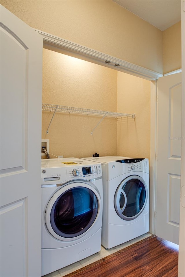 clothes washing area with laundry area, separate washer and dryer, and wood finished floors