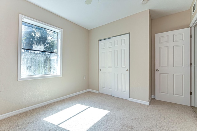 unfurnished bedroom featuring multiple windows, ceiling fan, a closet, and light carpet