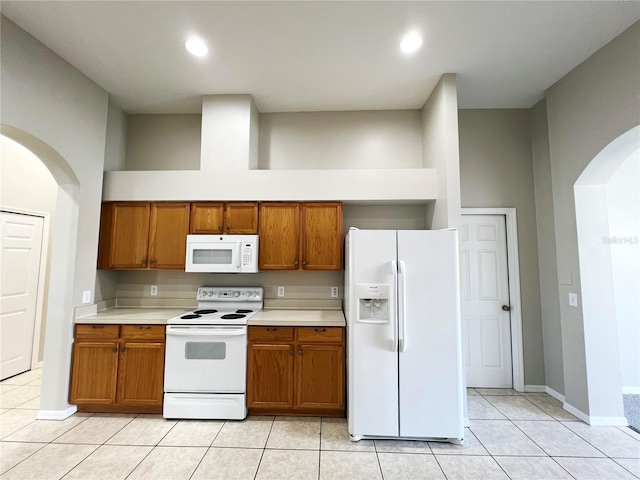 kitchen featuring a towering ceiling, white appliances, and light tile patterned flooring