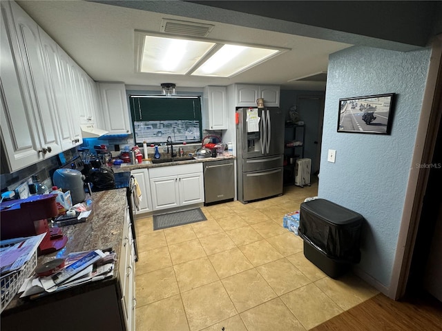 kitchen featuring radiator, white cabinetry, sink, stainless steel appliances, and light tile patterned floors