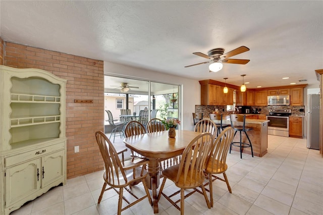 dining area with brick wall, light tile patterned floors, a textured ceiling, and ceiling fan