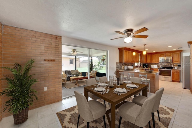 dining area with brick wall, sink, light tile patterned floors, ceiling fan, and a textured ceiling