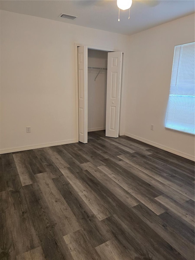 unfurnished bedroom with dark wood-style flooring, baseboards, visible vents, a ceiling fan, and a closet