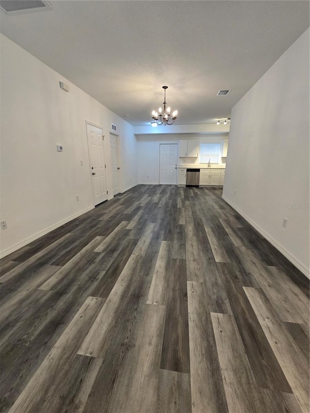 unfurnished living room with baseboards, visible vents, an inviting chandelier, and dark wood-style floors