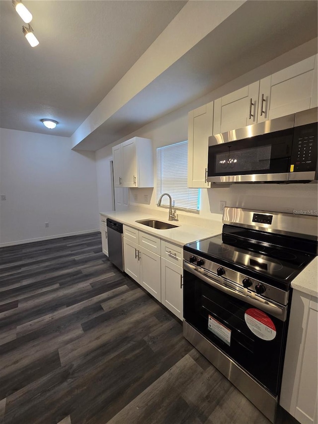 kitchen with stainless steel appliances, a sink, white cabinetry, light countertops, and dark wood-type flooring