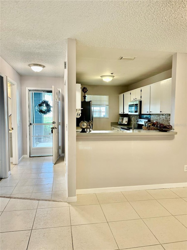 kitchen with a textured ceiling, light tile patterned floors, appliances with stainless steel finishes, kitchen peninsula, and white cabinets