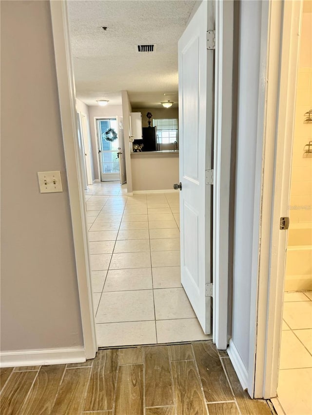 hallway with a textured ceiling and light tile patterned floors