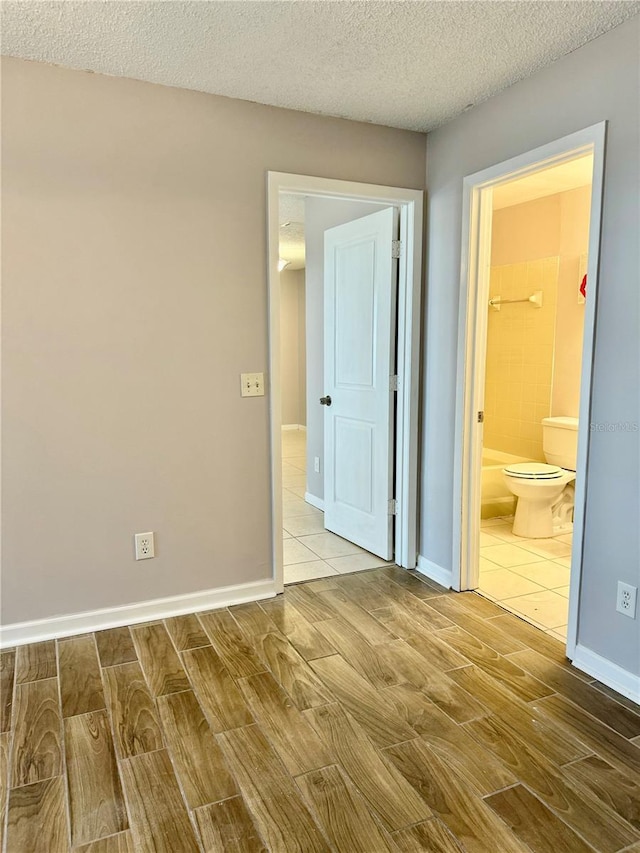 unfurnished bedroom featuring ensuite bath and a textured ceiling