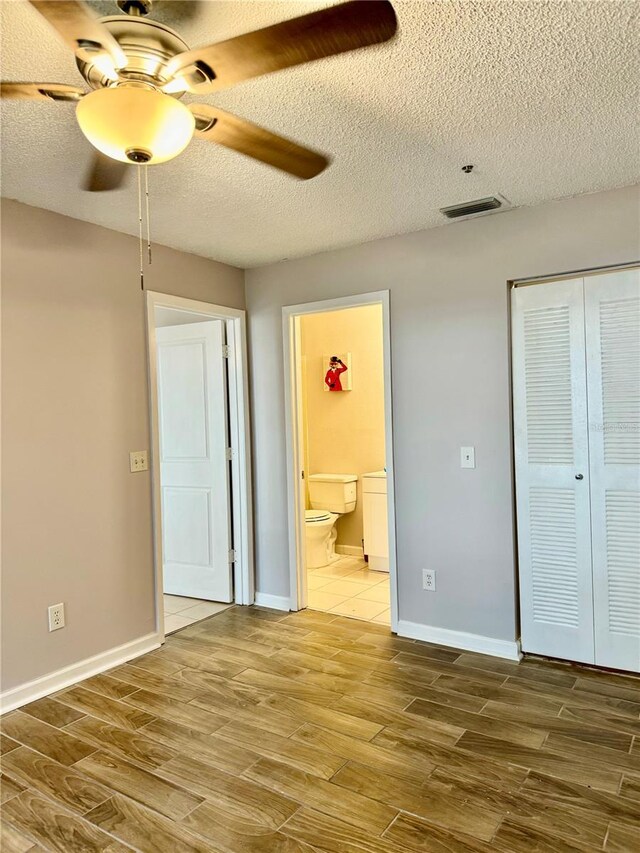 unfurnished bedroom with ensuite bathroom, wood-type flooring, a textured ceiling, a closet, and ceiling fan