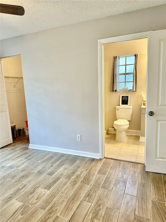 unfurnished bedroom with ensuite bath, a textured ceiling, and a walk in closet