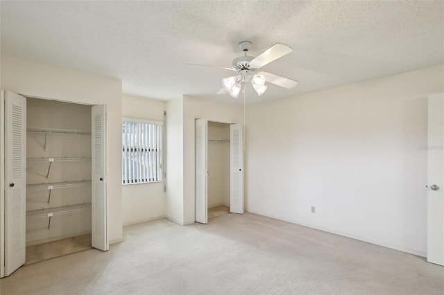 unfurnished bedroom featuring light carpet, two closets, ceiling fan, and a textured ceiling