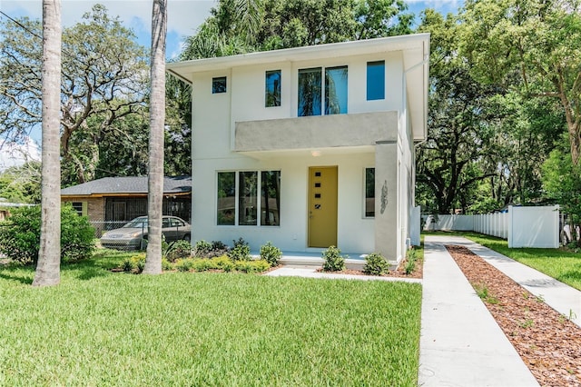 contemporary house featuring stucco siding, a front lawn, driveway, and fence